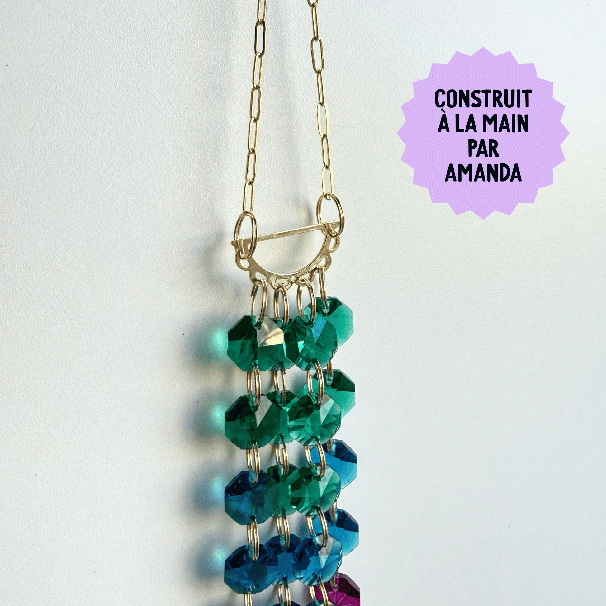 beaded suncatcher with green and blue beads on a white background, labeled 'Construit  La Main Par Amanda'.